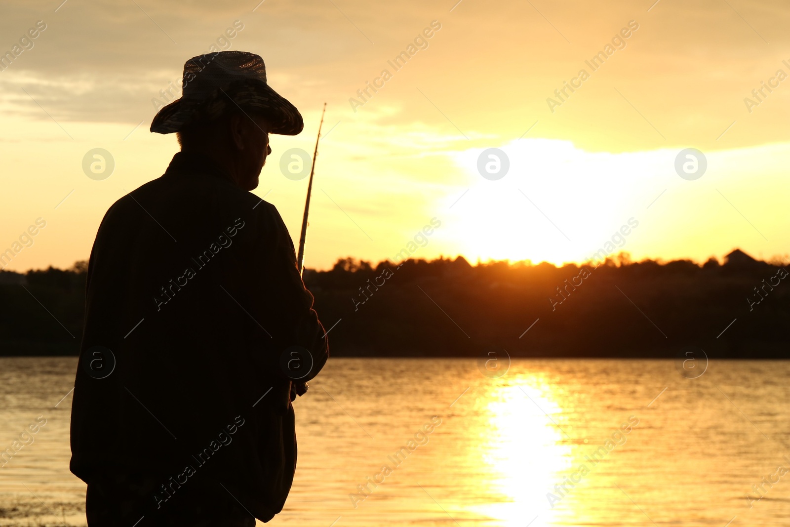 Photo of Fisherman with rod fishing near lake at sunset. Space for text