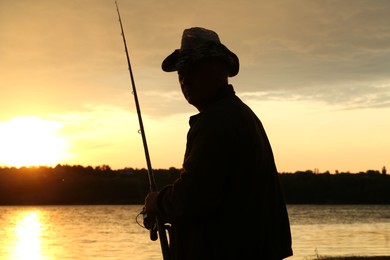 Fisherman with rod fishing near lake at sunset