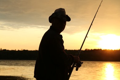 Photo of Fisherman with rod fishing near lake at sunset