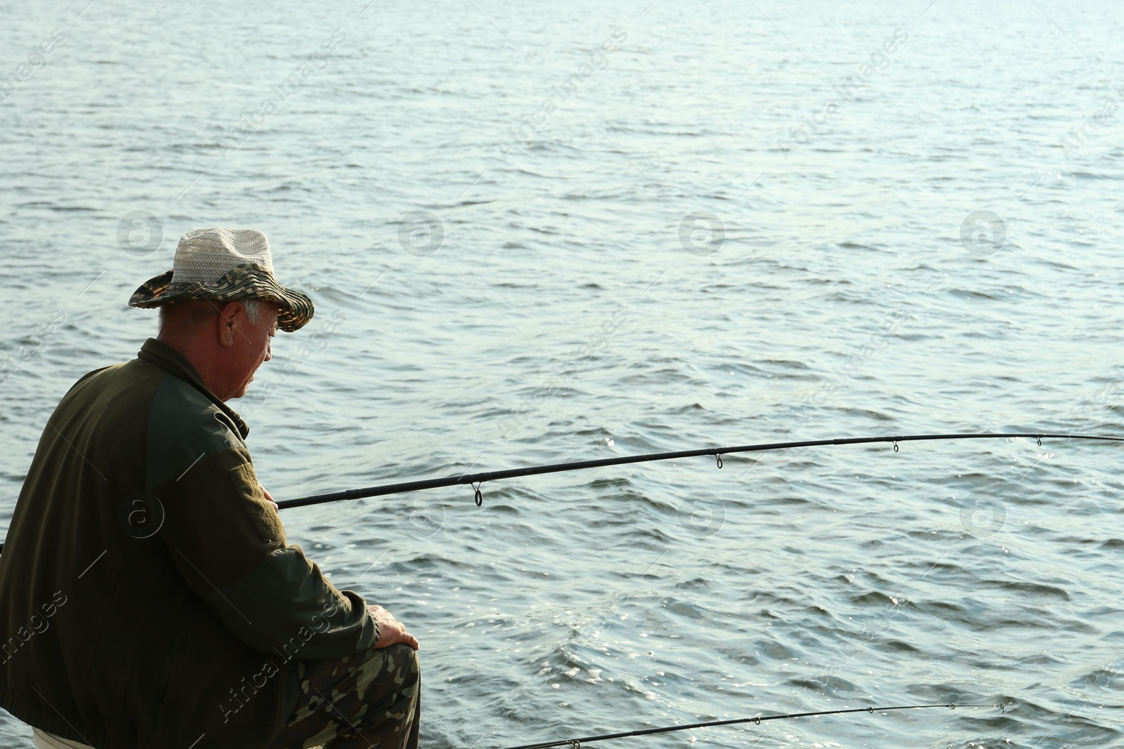 Photo of Fisherman with rod fishing near lake at summer. Space for text