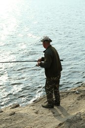 Photo of Fisherman with rod fishing near lake at summer, back view