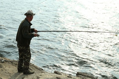 Fisherman with rod fishing near lake at summer, back view