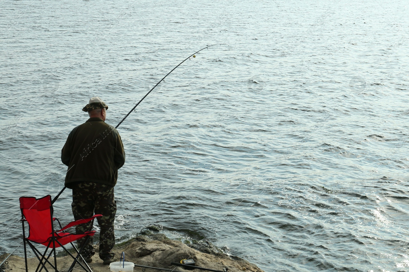 Photo of Fisherman with rod fishing near lake at summer, back view. Space for text