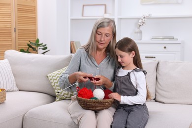 Photo of Grandmother teaching her granddaughter to knit on sofa at home