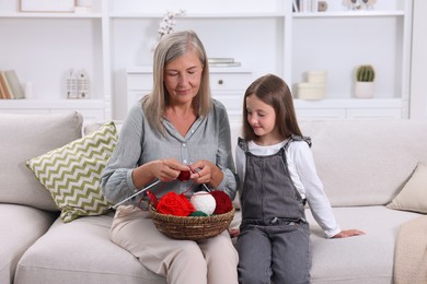 Photo of Grandmother teaching her granddaughter to knit on sofa at home