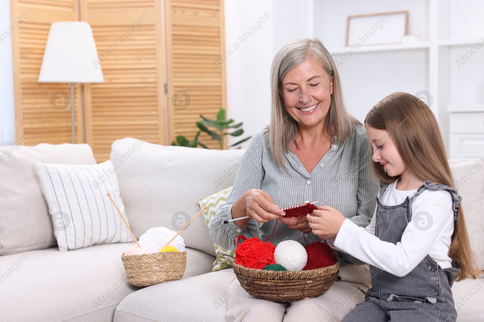 Photo of Smiling grandmother teaching her granddaughter to knit on sofa at home. Space for text