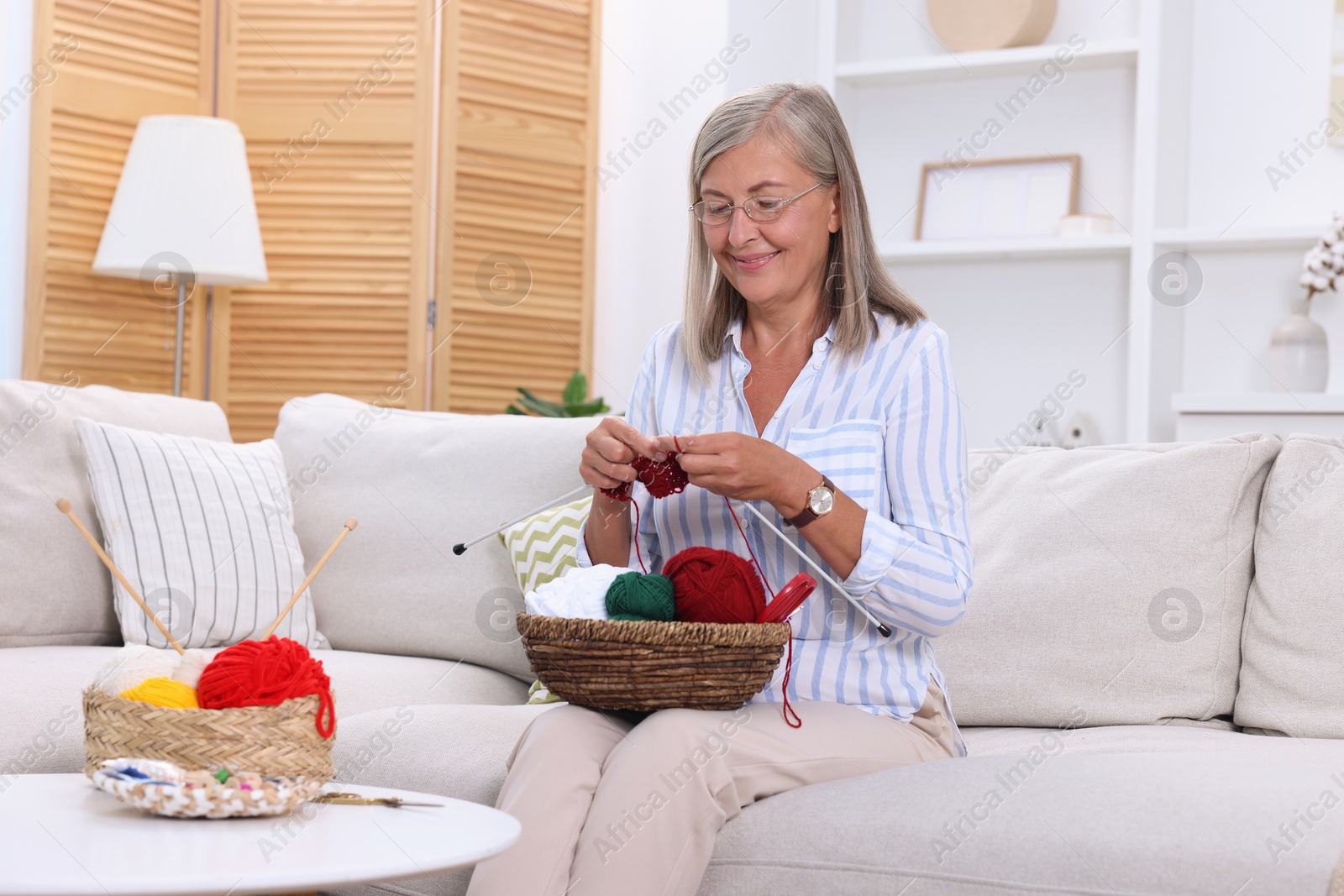 Photo of Woman with basket of yarn knitting on sofa at home