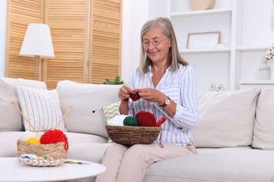 Woman with basket of yarn knitting on sofa at home