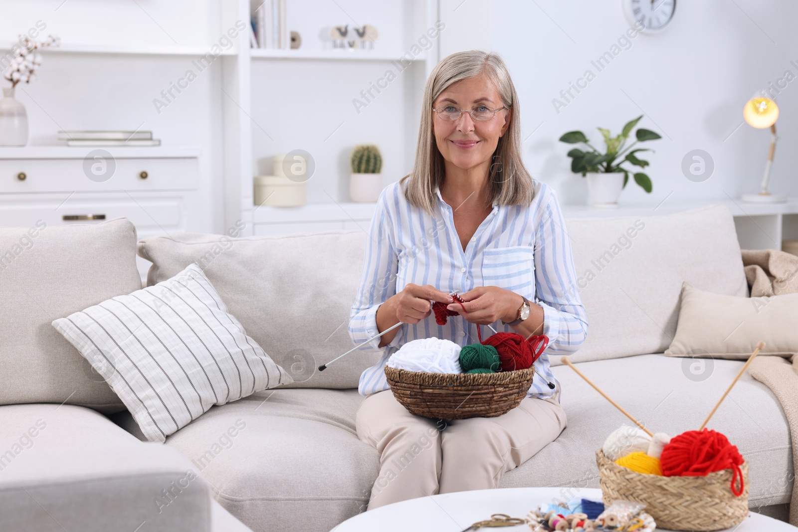 Photo of Woman with basket of yarn knitting on sofa at home