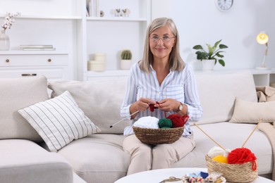 Photo of Woman with basket of yarn knitting on sofa at home