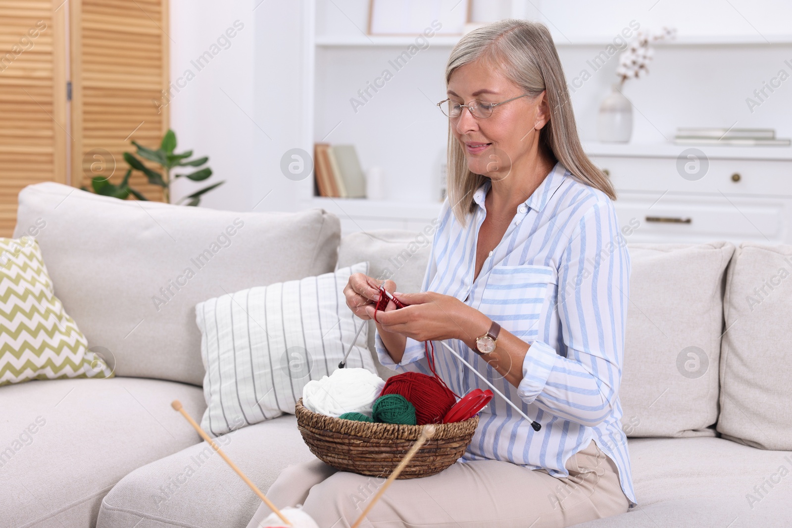 Photo of Woman with basket of yarn knitting on sofa at home