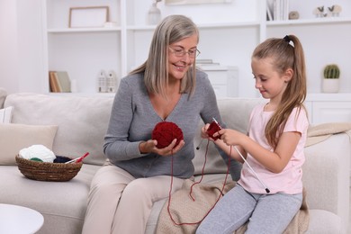 Photo of Smiling grandmother teaching her granddaughter to knit on sofa at home