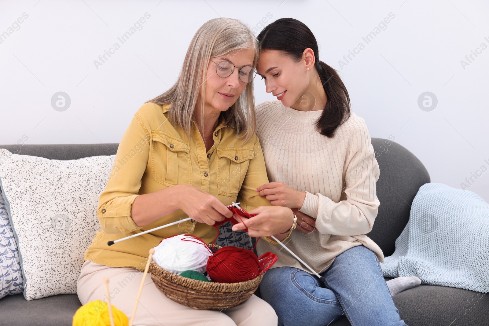 Photo of Smiling daughter observing her mother knitting on sofa at home