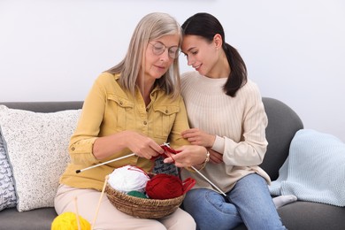 Smiling daughter observing her mother knitting on sofa at home