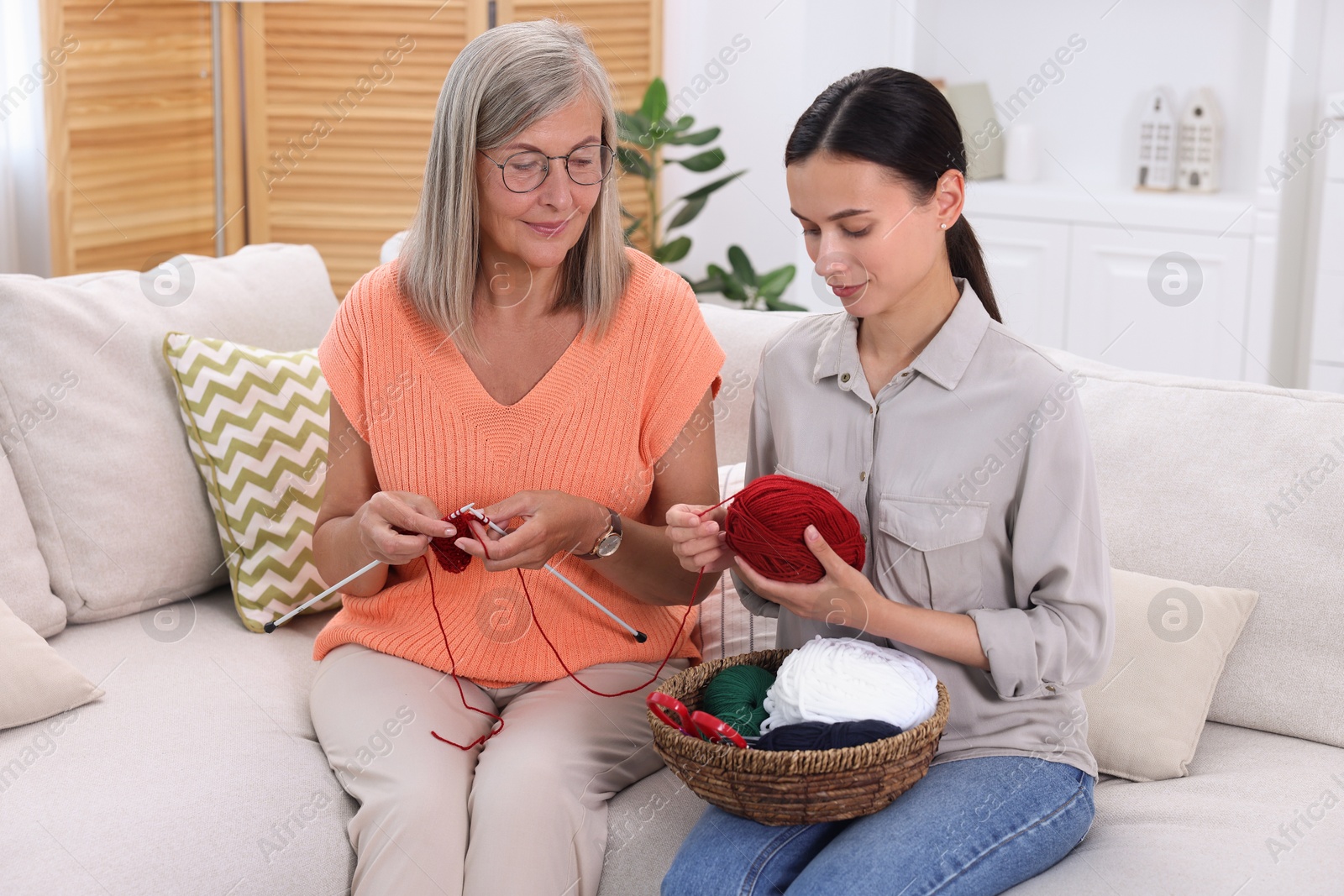 Photo of Mother and daughter with skeins of yarn spending time together on sofa at home