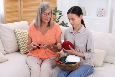 Mother and daughter with skeins of yarn spending time together on sofa at home