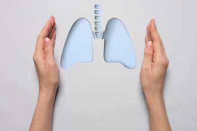 Image of Woman holding hands near lungs paper cutout on white background, closeup. Asthma and other respiratory diseases