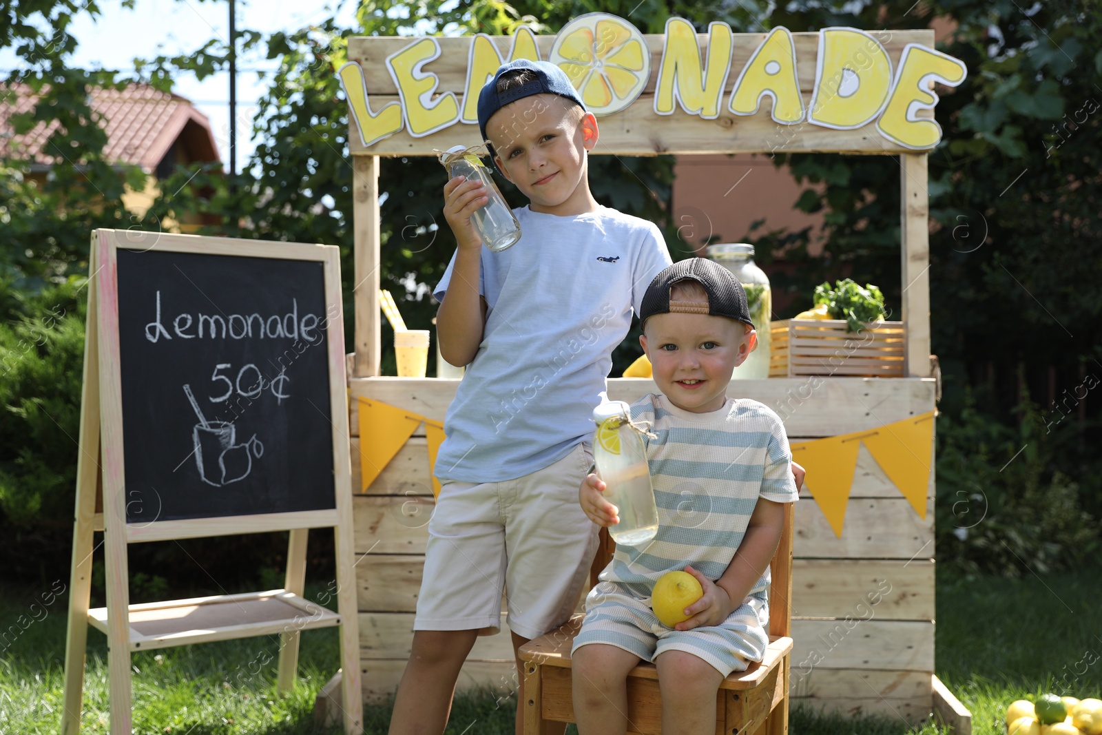 Photo of Cute boys with refreshing drinks near lemonade stand in park