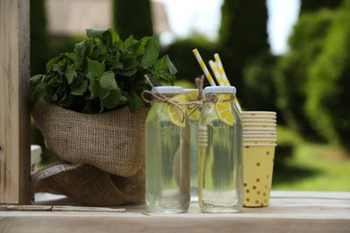 Refreshing natural lemonade in bottles and mint on wooden stand outdoors