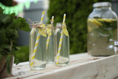 Refreshing natural lemonade in bottles and mint on wooden stand outdoors