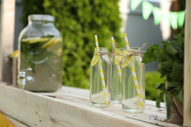 Photo of Refreshing natural lemonade in bottles and mint on wooden stand outdoors