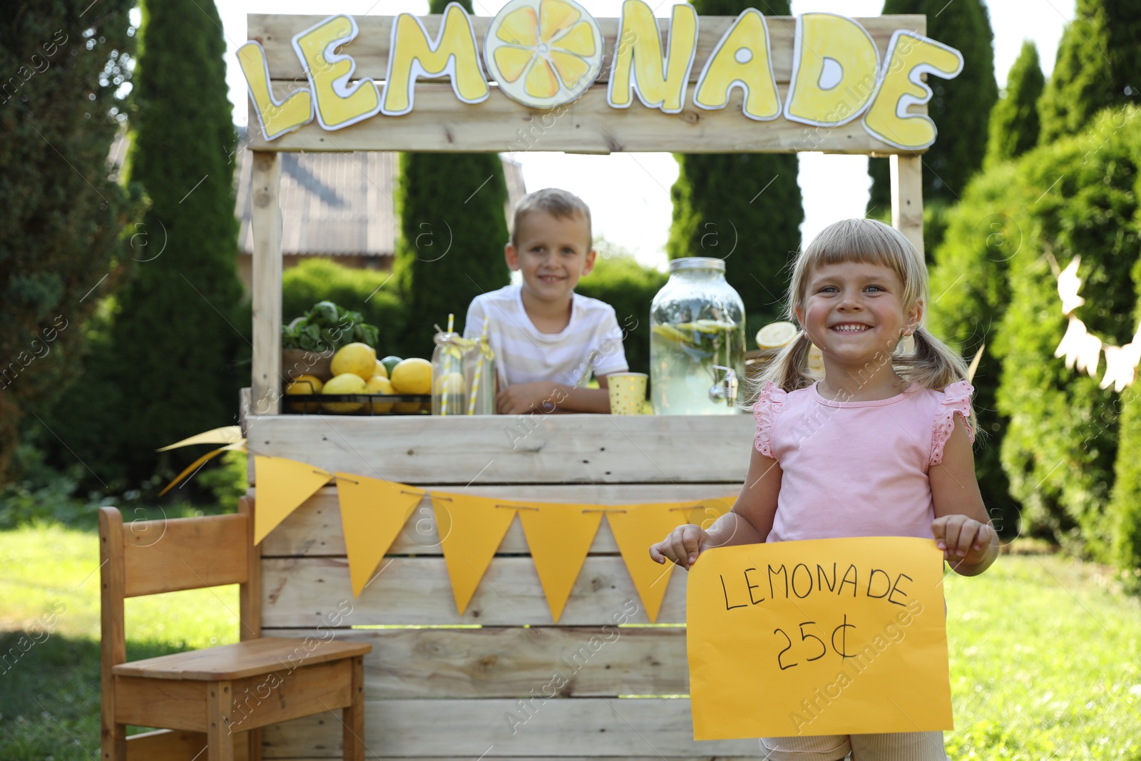 Photo of Little girl holding price tag near lemonade stand in park