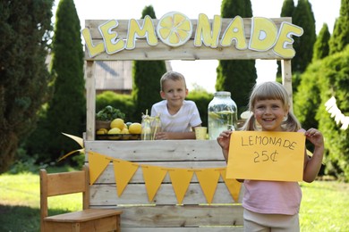 Photo of Little girl holding price tag near lemonade stand in park