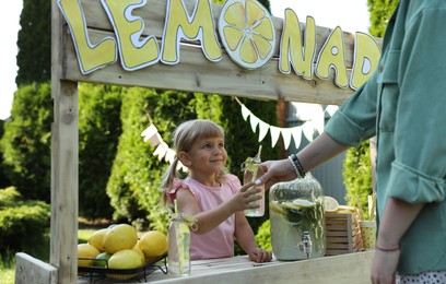 Photo of Cute little girl selling natural lemonade to woman in park