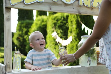 Cute little boy selling natural lemonade to woman in park