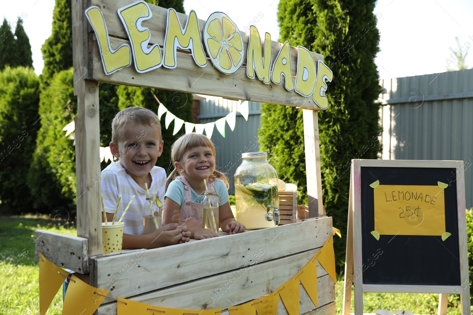 Photo of Cute little kids with refreshing drinks at lemonade stand in park