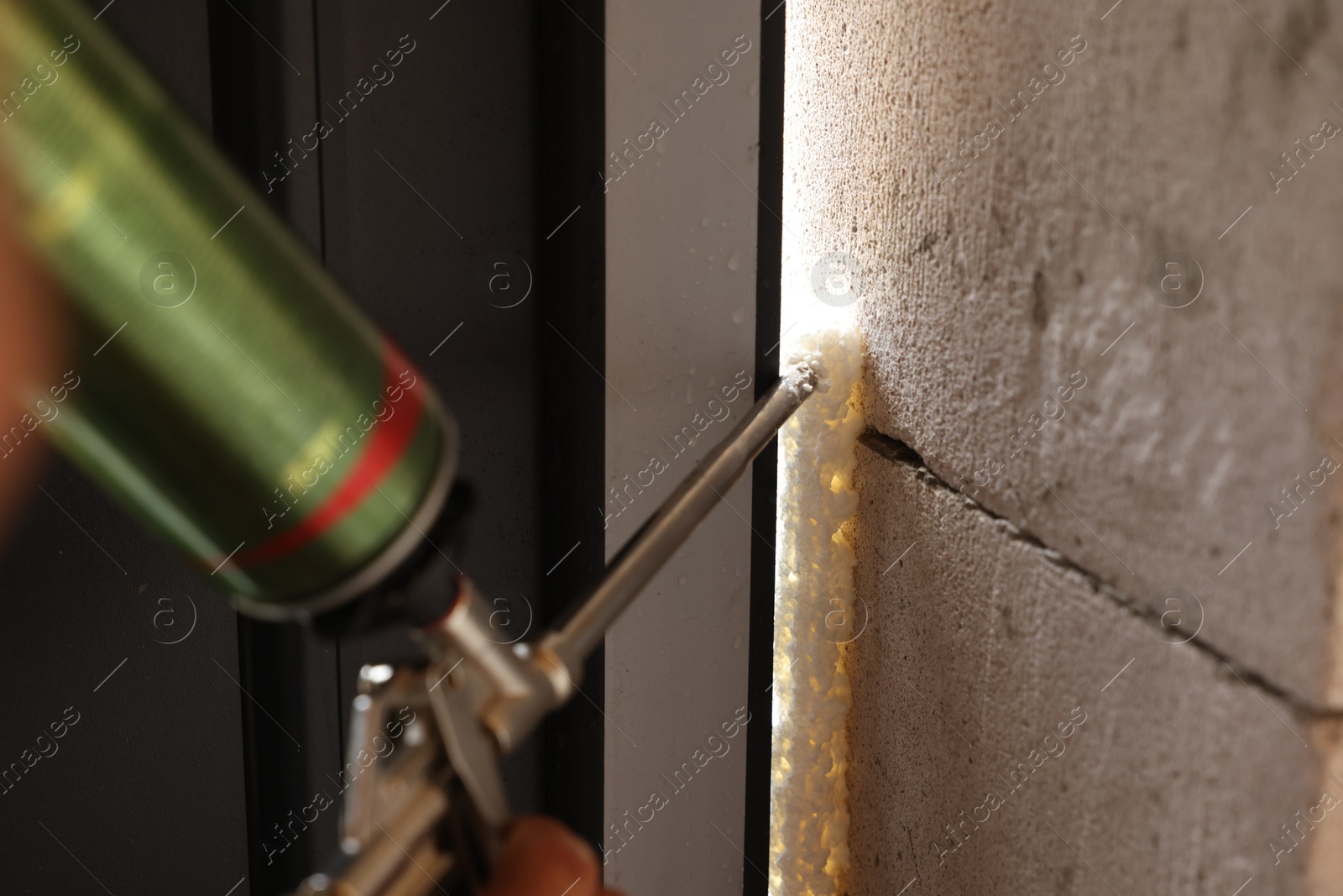 Photo of Repairman with polyurethane foam insulating new door at home, closeup