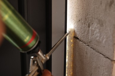 Photo of Repairman with polyurethane foam insulating new door at home, closeup