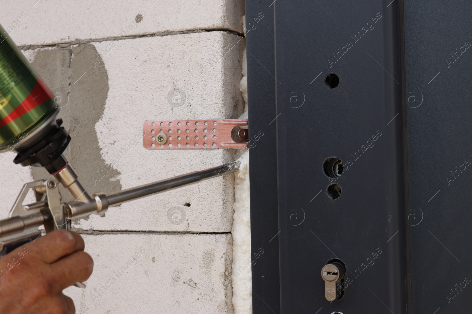 Photo of Repairman with polyurethane foam insulating new door at home, closeup