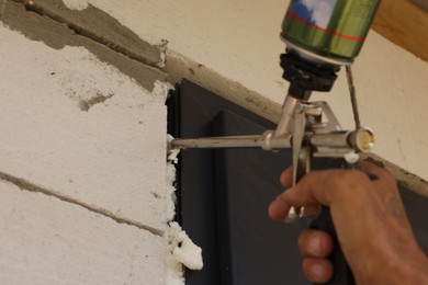 Photo of Repairman with polyurethane foam insulating new door at home, closeup