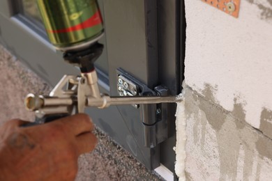 Photo of Repairman with polyurethane foam insulating new door at home, closeup