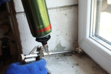 Photo of Repairman with polyurethane foam insulating new window at home, closeup