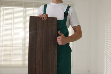 Photo of Worker with samples of wooden flooring showing thumbs up indoors, closeup