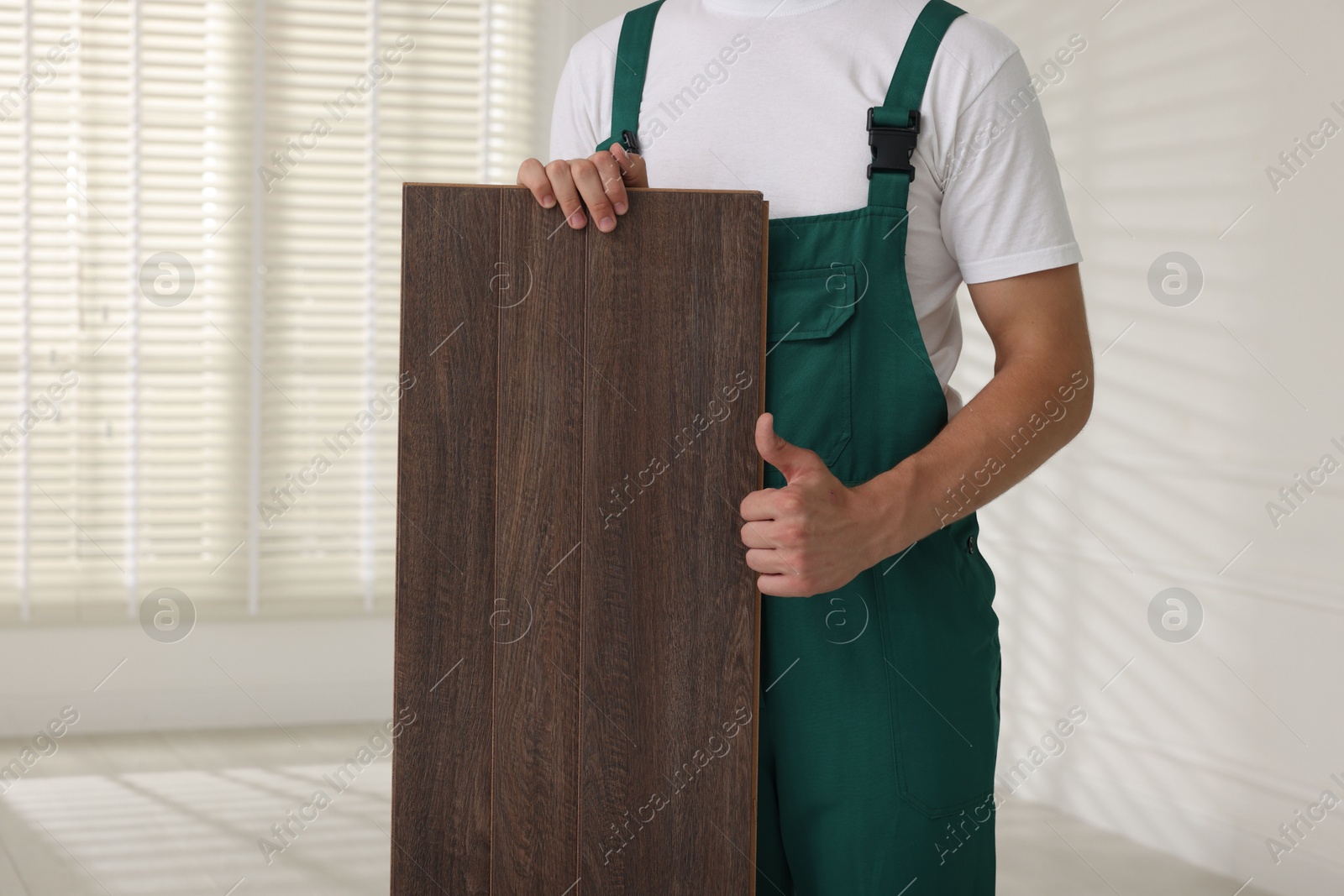 Photo of Worker with samples of wooden flooring showing thumbs up indoors, closeup