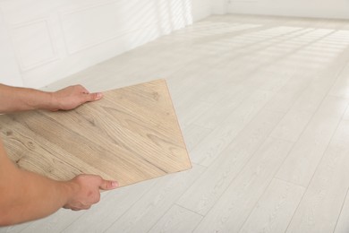 Photo of Man with sample of wooden flooring indoors, closeup. Space for text