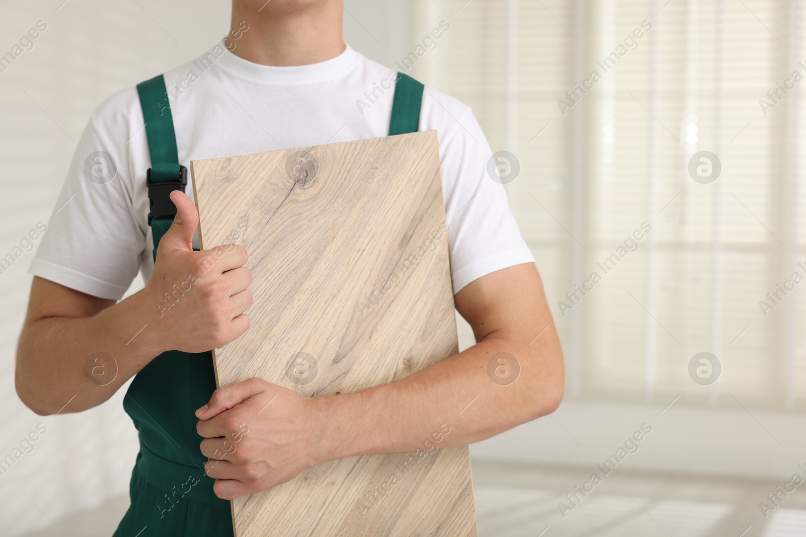 Photo of Man with sample of wooden flooring showing thumbs up indoors, closeup