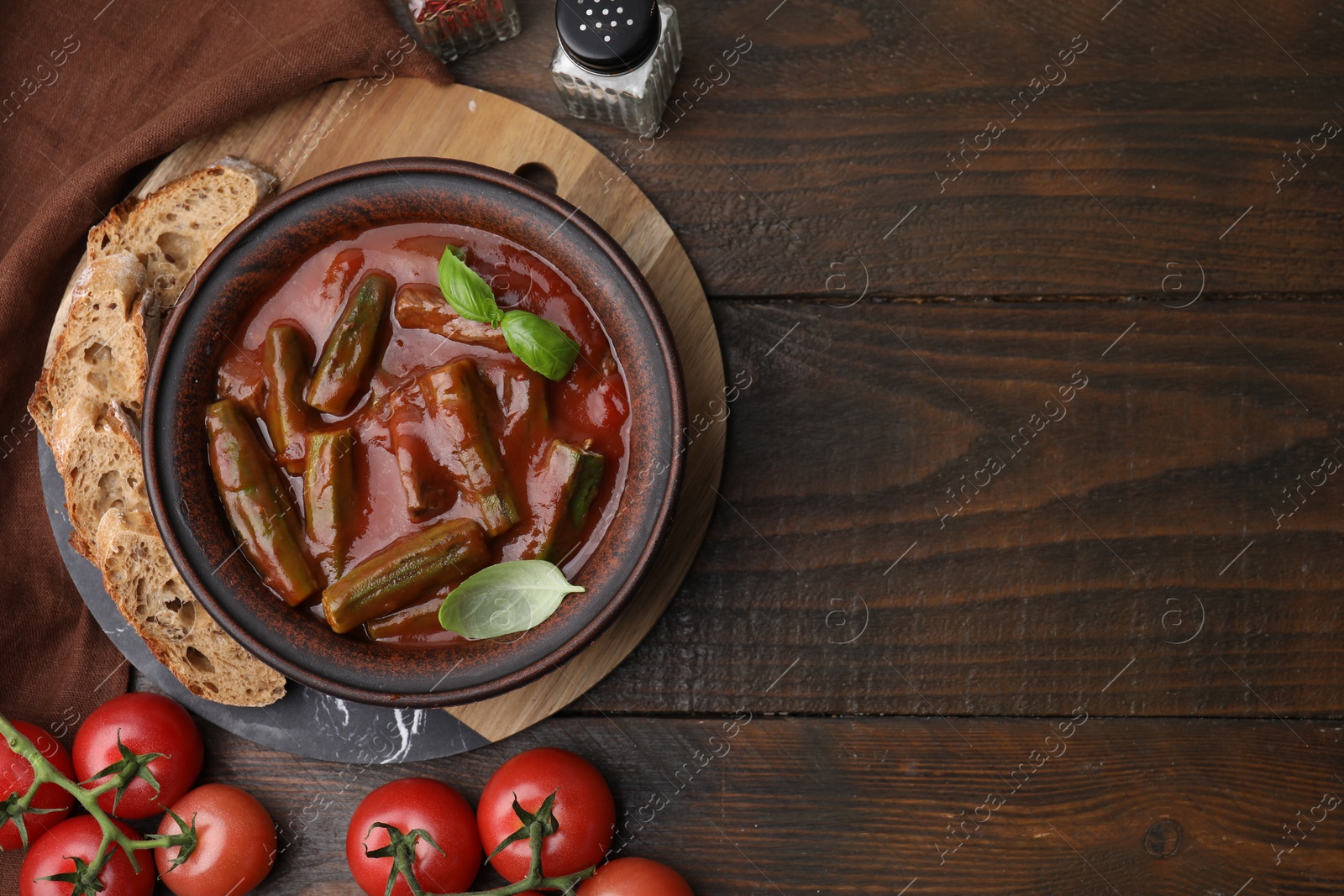 Photo of Tasty stew with okra, tomato sauce, bread and basil on wooden table, flat lay