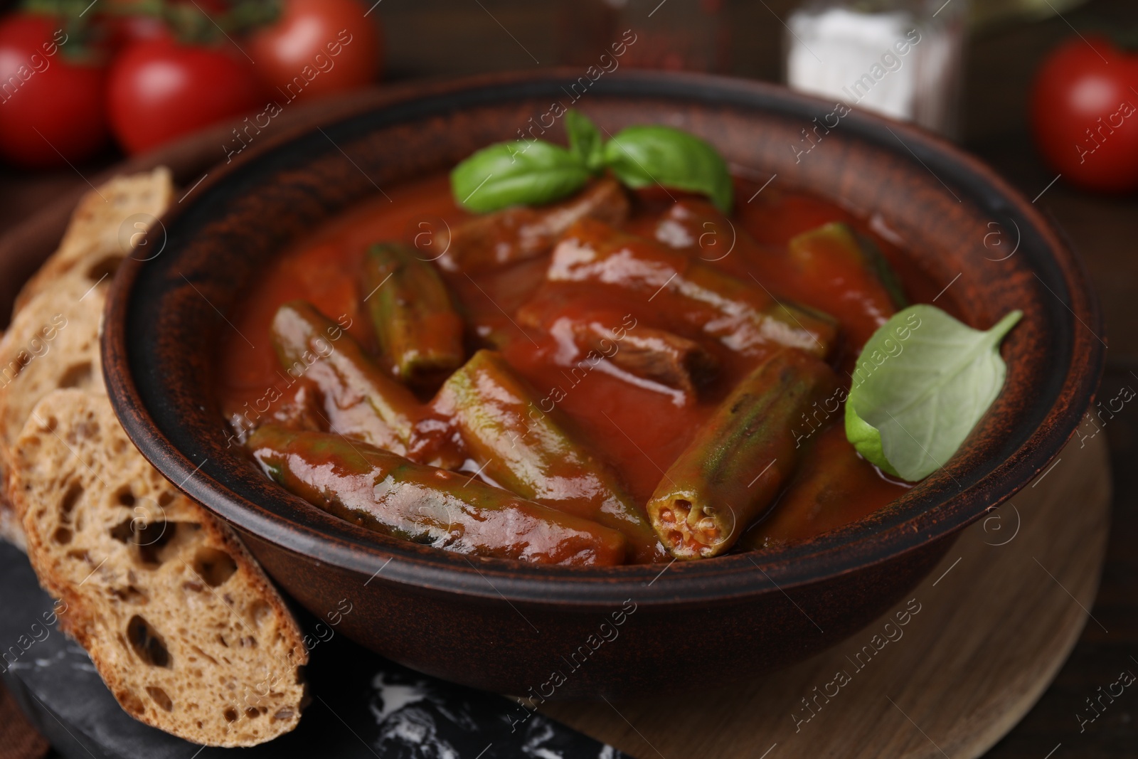 Photo of Tasty stew with okra, tomato sauce, bread and basil on wooden table, closeup