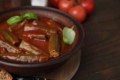 Photo of Tasty stew with okra, tomato sauce and basil on wooden table, closeup. Space for text