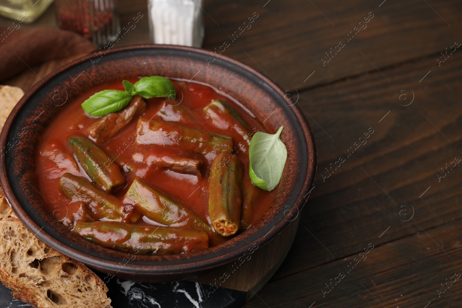 Photo of Tasty stew with okra, tomato sauce, bread and basil on wooden table, space for text