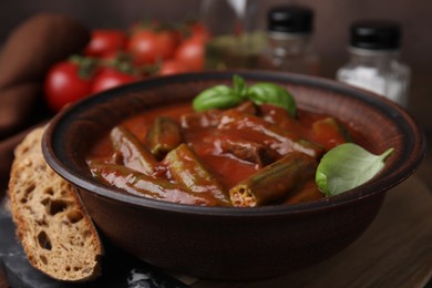 Photo of Tasty stew with okra, tomato sauce, bread and basil on wooden table, closeup