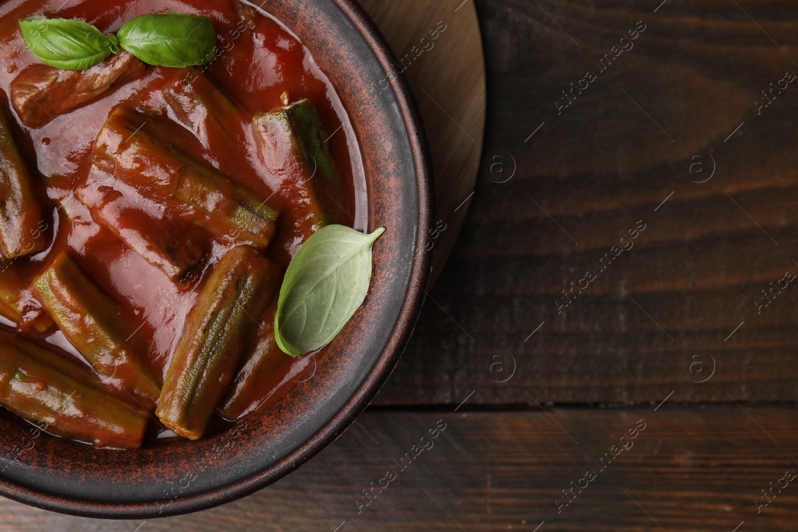 Photo of Tasty stew with okra, tomato sauce and basil on wooden table, top view. Space for text