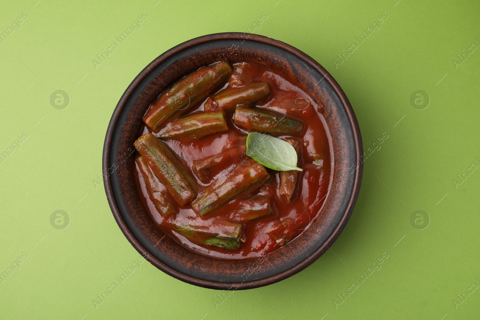 Photo of Tasty stew with okra, tomato sauce and basil on light green background, top view