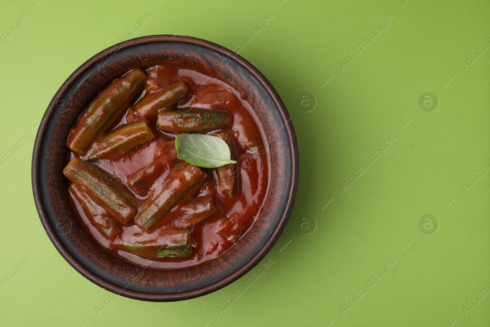 Photo of Tasty stew with okra, tomato sauce and basil on light green background, top view. Space for text