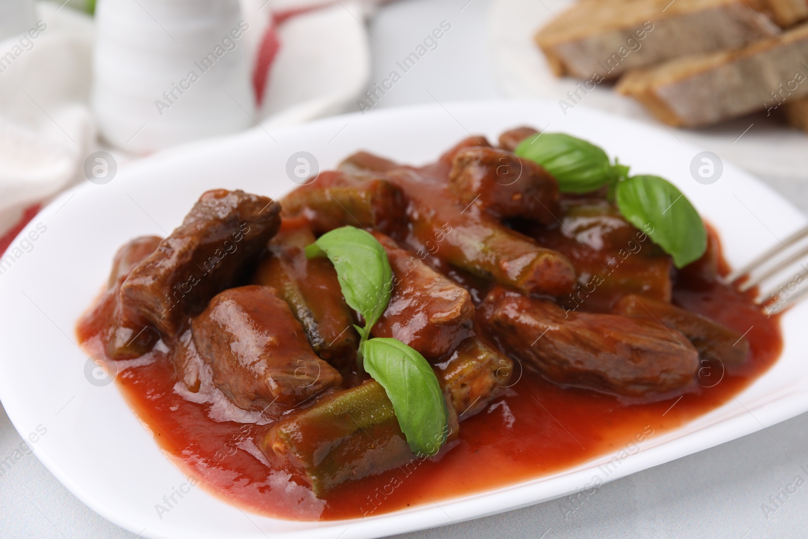 Photo of Tasty stew with okra, tomato sauce and basil on white tiled table, closeup