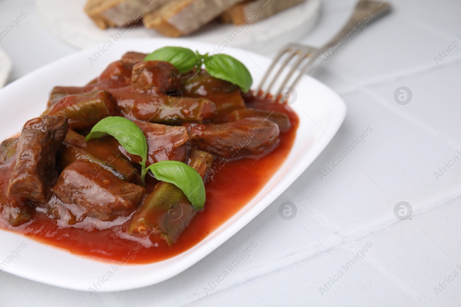 Photo of Tasty stew with okra, tomato sauce and basil on white tiled table, closeup. Space for text